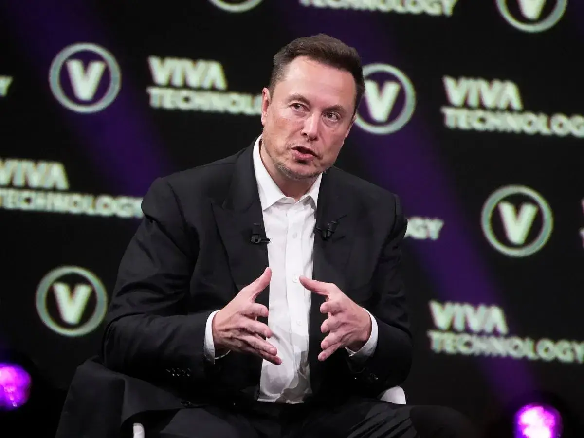 Elon Musk w czarnym garniturze, gestykuluje podczas panelu Viva Technology.