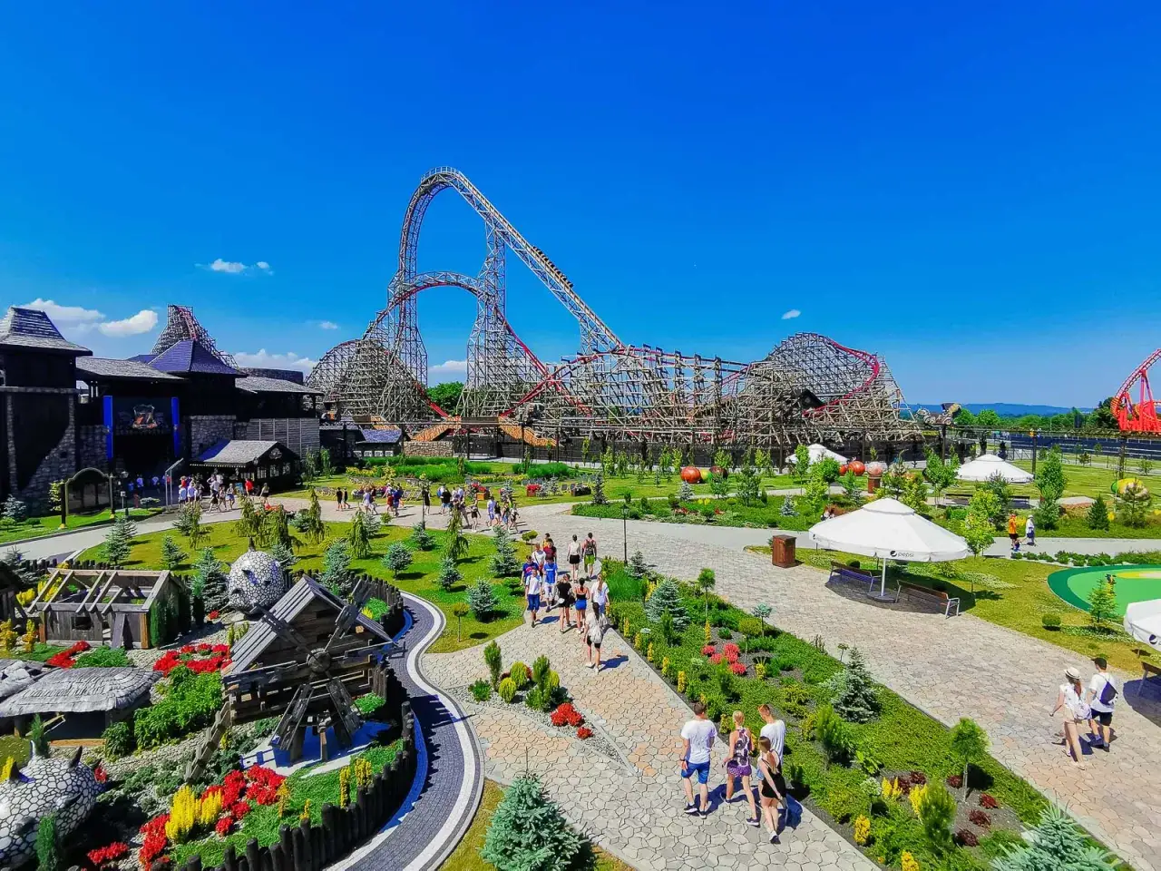 Energylandia Zator atrakcje: drewniane rollercoastery, zamki, wiatrak i zielone alejki pełne spacerujących ludzi.