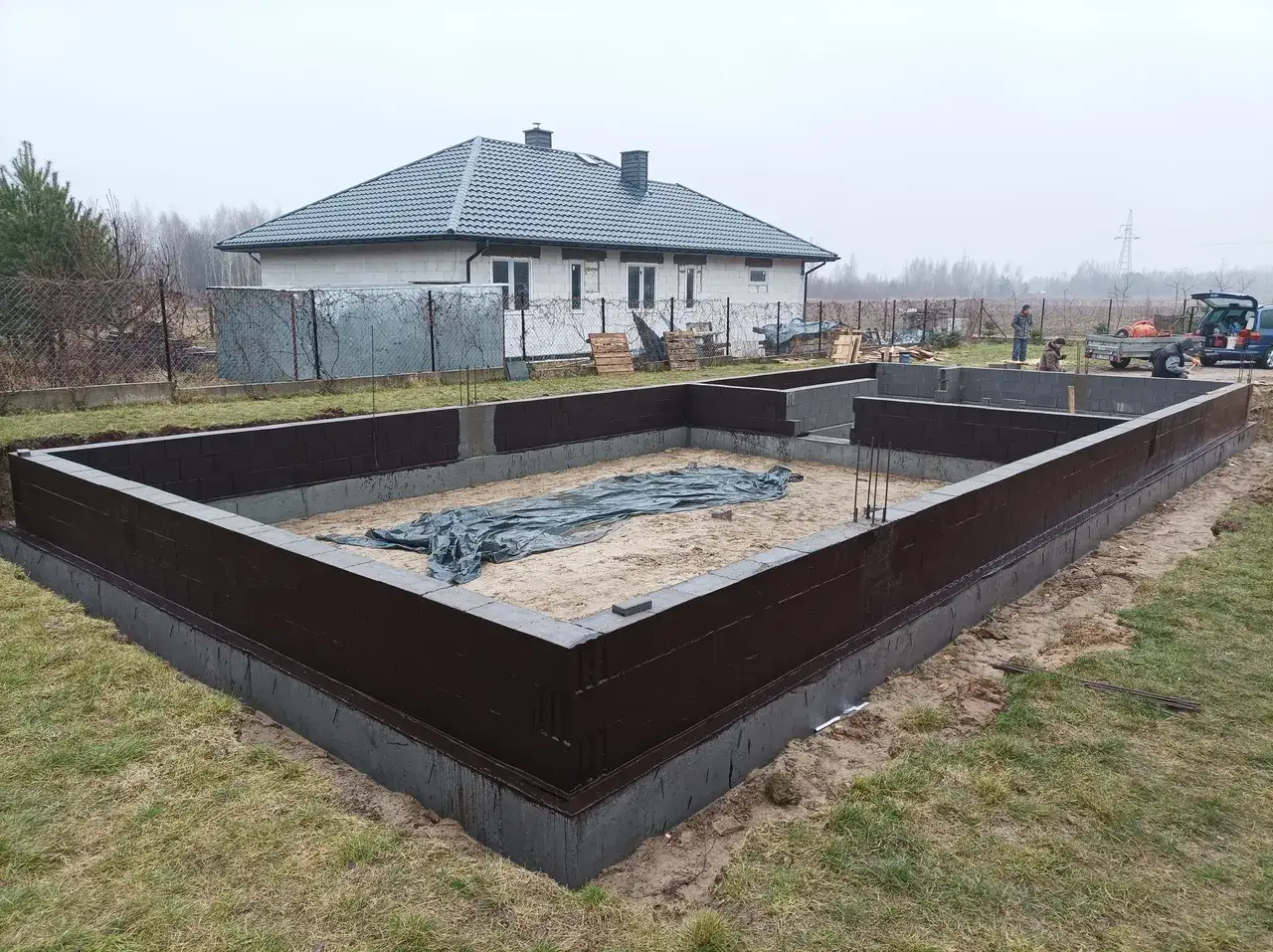 Fundament domu w budowie, ciemnobrązowy cokolik z bloczków betonowych, gotowy na dalsze prace.