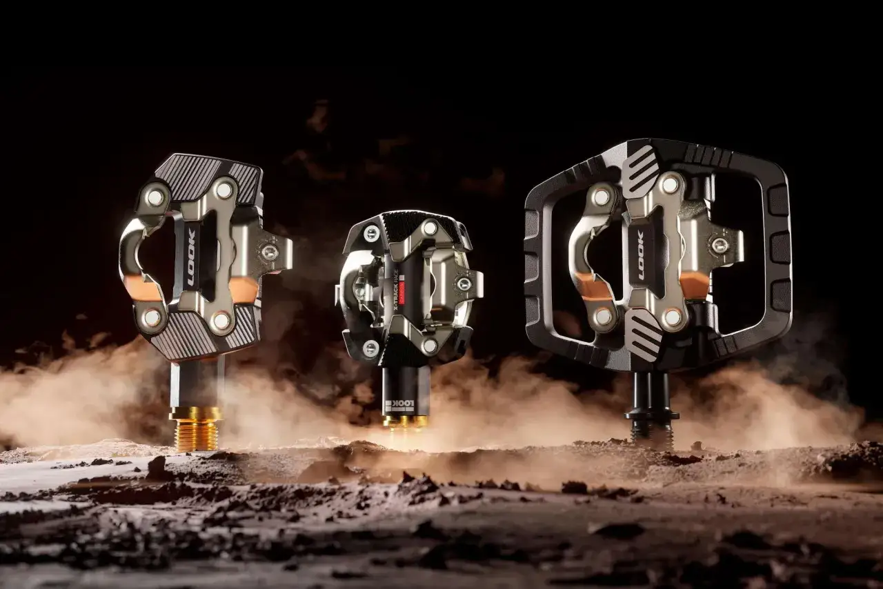 Trzy pedały LOOK X-Track, idealne do gravela, prezentują się na tle pyłu i ciemności.