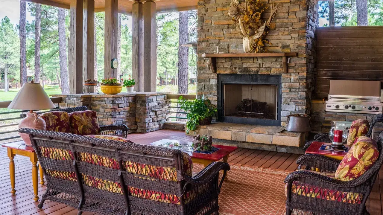 Przytulny taras z kamienia i drewna, z wygodnymi meblami i grillem, otoczony lasem.