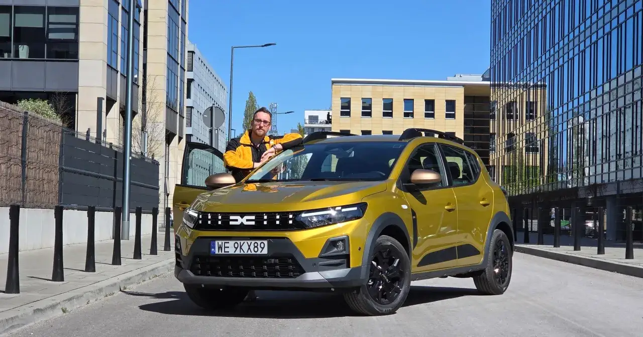 Mężczyzna opiera się o żółtego Dacia Sandero Stepway. Zastanawia się nad jego spalaniem podczas miejskiej jazdy.