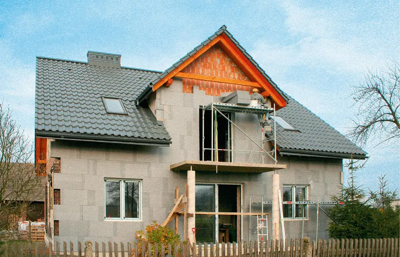 Trwa ocieplenie starego domu. Robotnik na rusztowaniu montuje bloczki na elewacji.