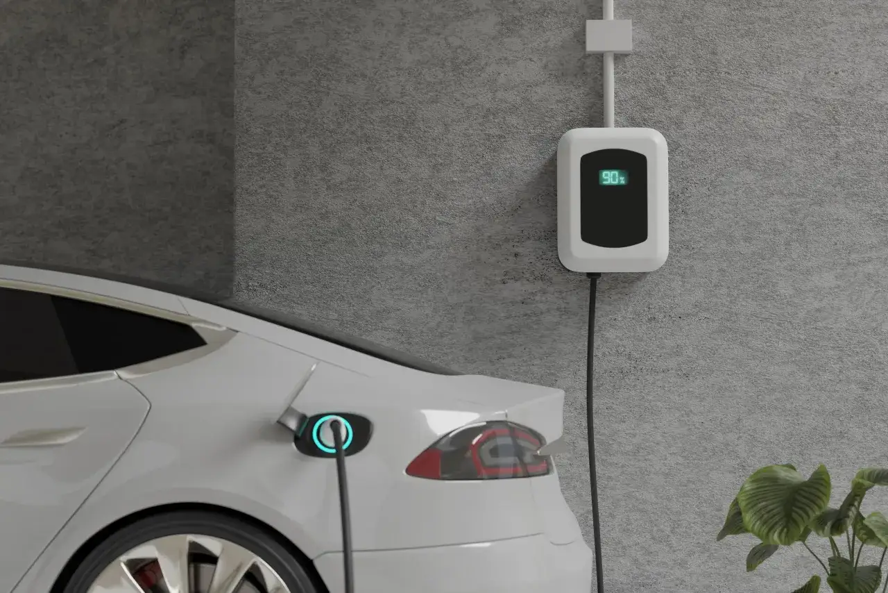 Biały samochód elektryczny jest podłączony do ładowarki ściennej, która pokazuje 90%. Ładowanie samochodu elektrycznego w domu to wygodne rozwiązanie.