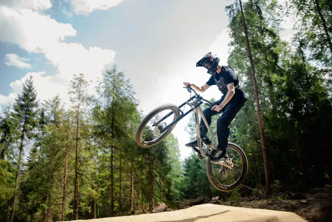 Rowerzysta w kasku wykonuje skok w lesie, szukając najlepszych bike parków w Polsce.