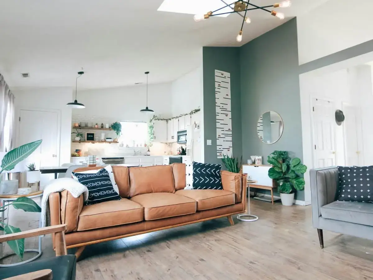 Nowoczesny salon z brązową kanapą i szarą sofą. Ściana pomalowana do połowy na zielono, z ozdobnym wzrostomierzem.