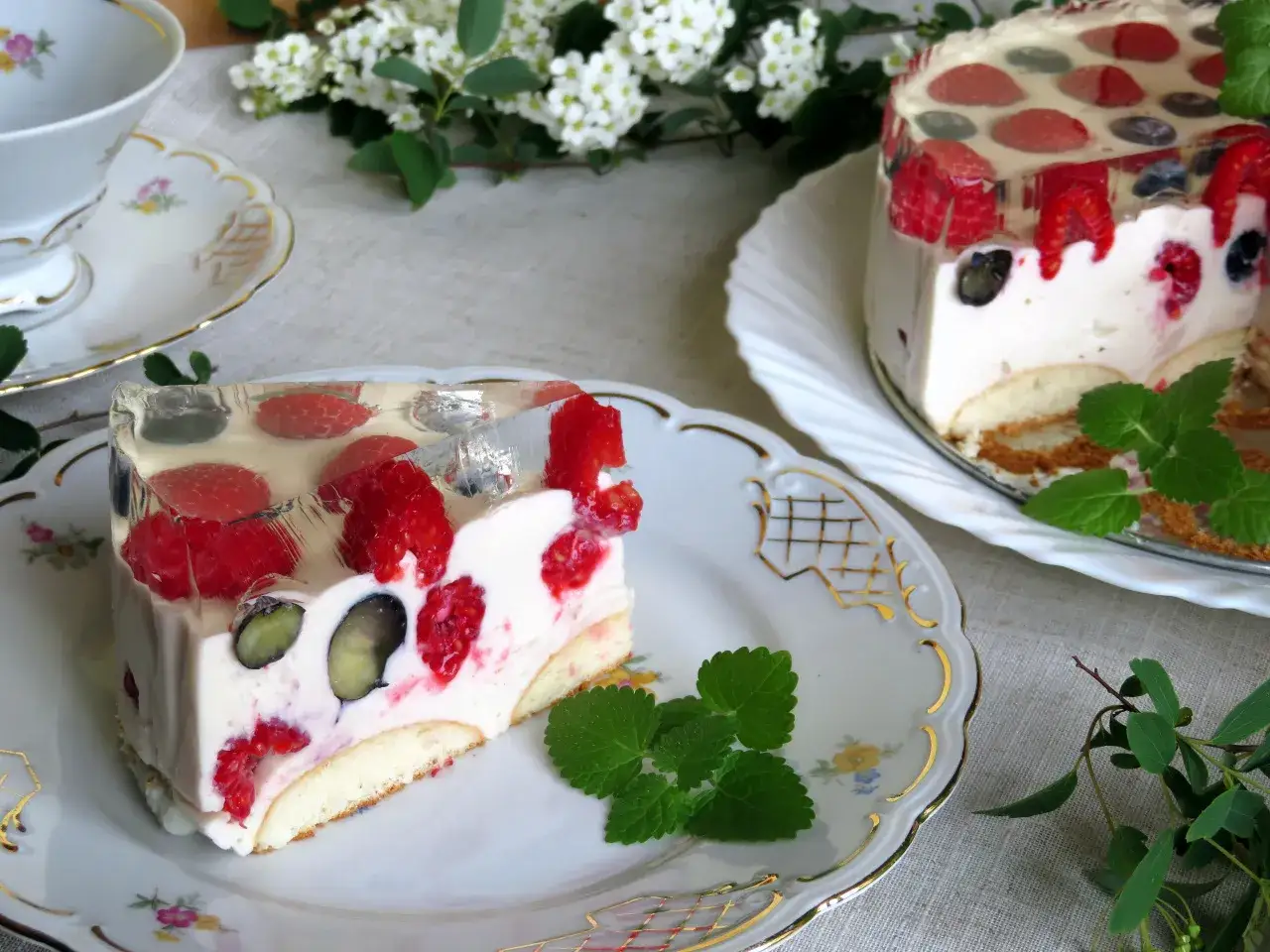 Pyszne ciasto budyniowe bez pieczenia z malinami i borówkami w galaretce, podane na eleganckim talerzyku.