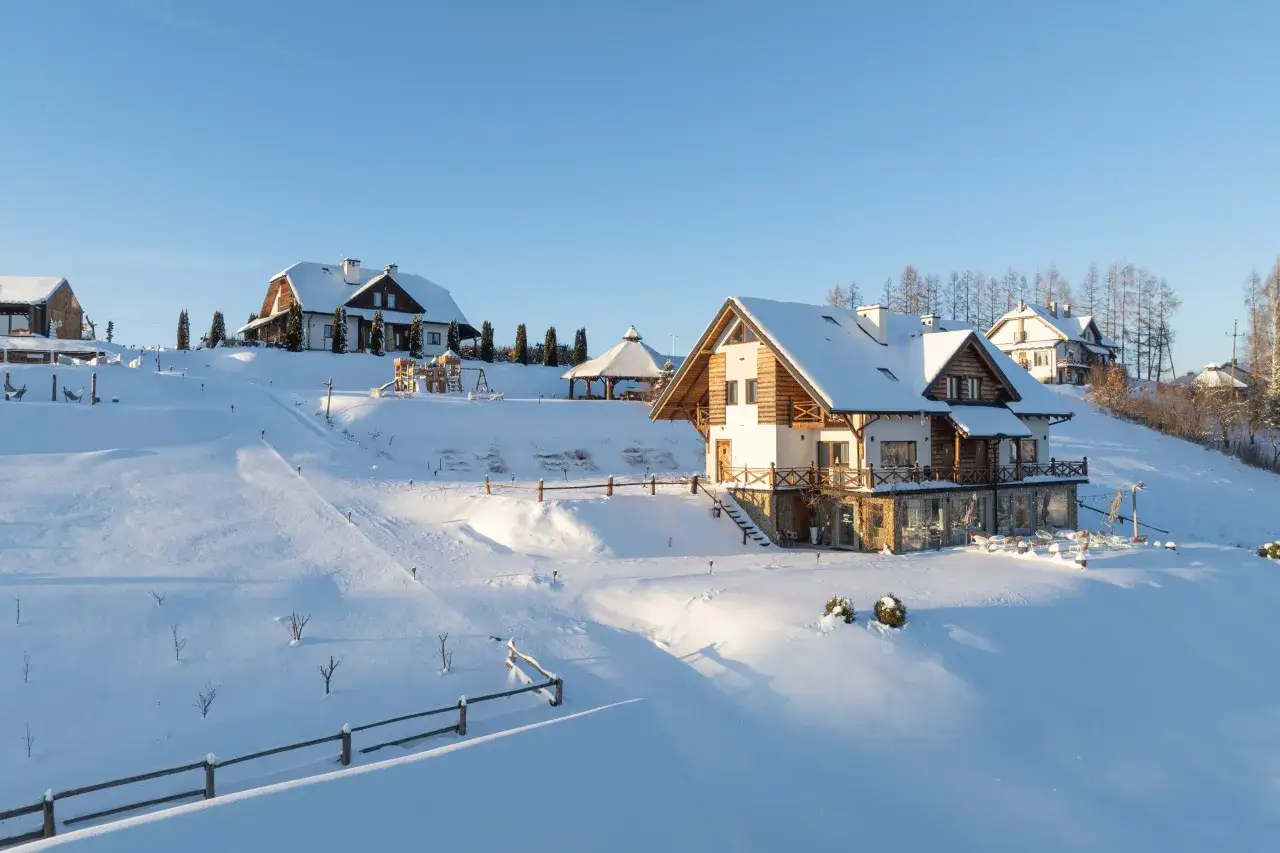 Idealne miejsca na ferie zimowe: ośnieżone domy z drewna i kamienia, plac zabaw, altana i leżaki czekają na gości.