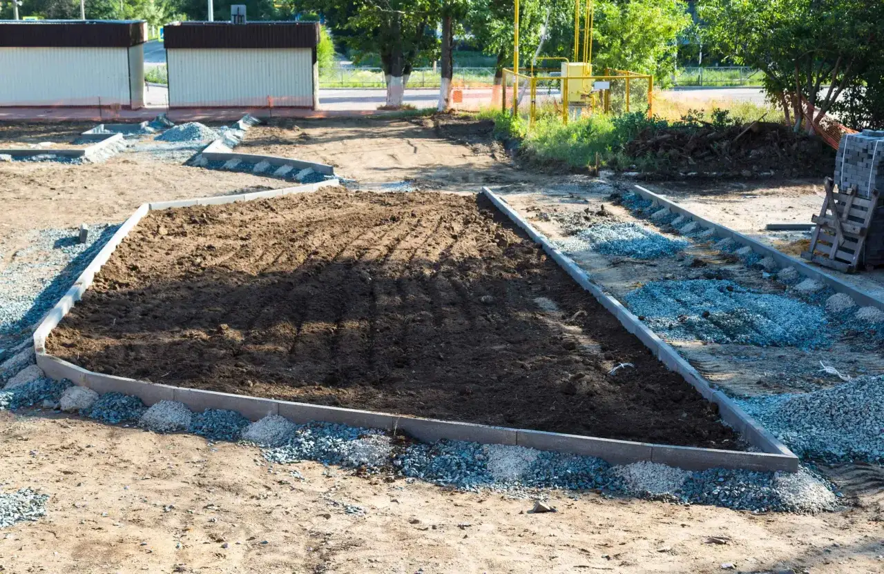 Przygotowanie terenu pod rabatę, widoczne obrzeże i kruszywo. Widać etapy jak zrobić obrzeże z cegły, choć tu użyto betonowych krawężników.