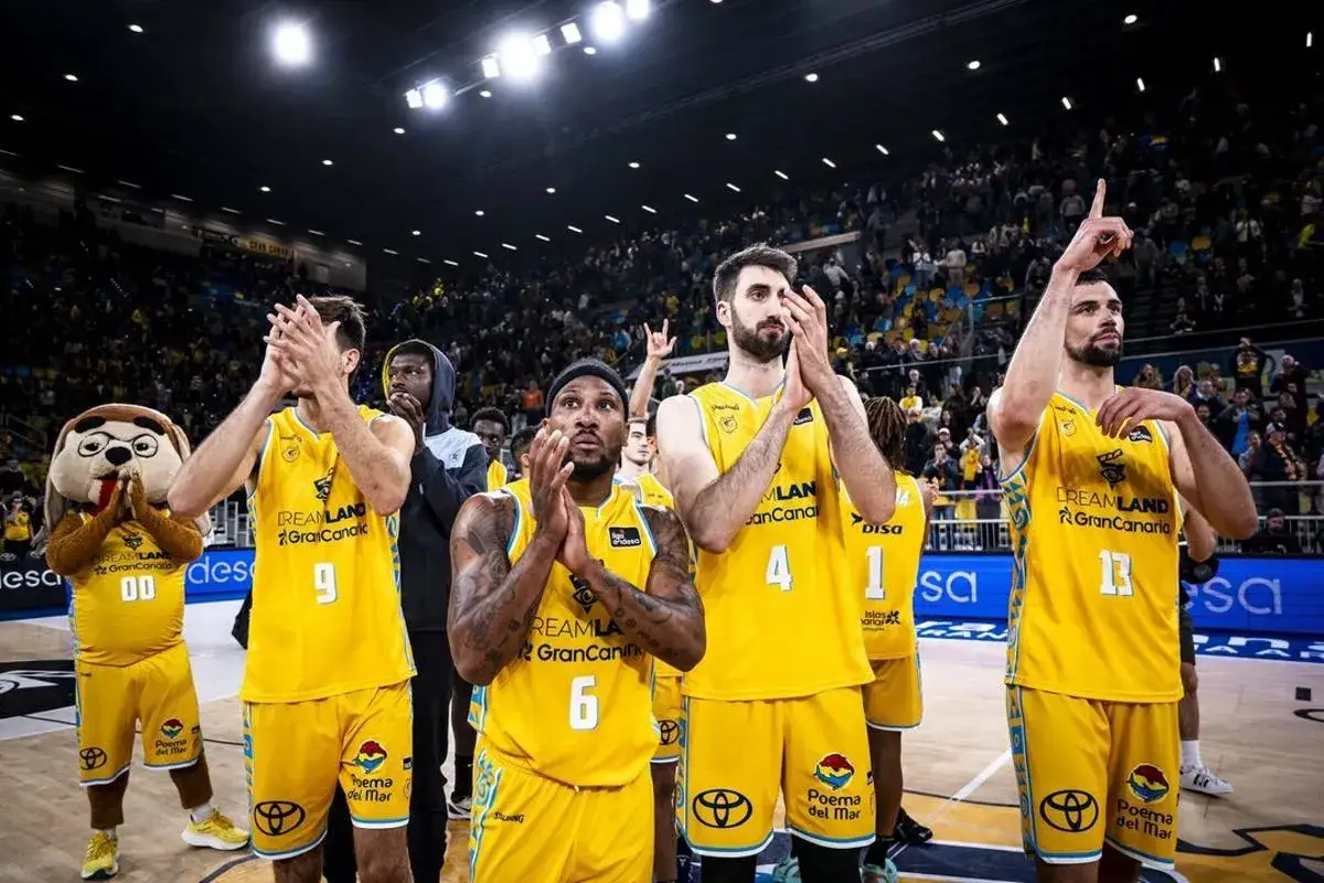 Jugadores del club baloncesto Gran Canaria, con sus uniformes amarillos, aplauden ante una multitud.