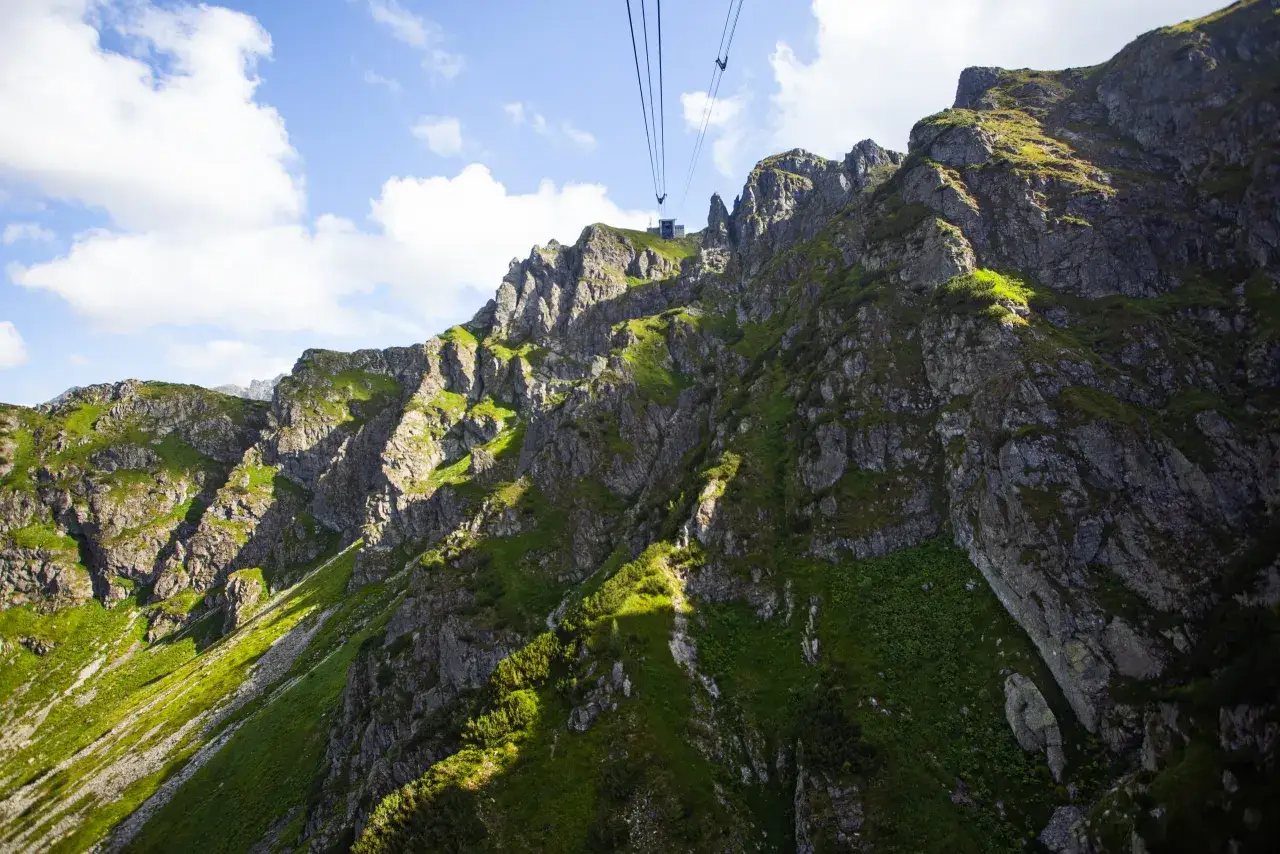 Widok na skaliste zbocza i zielone hale Tatr, z widoczną kolejką linową wjeżdżającą na Kasprowy Wierch.