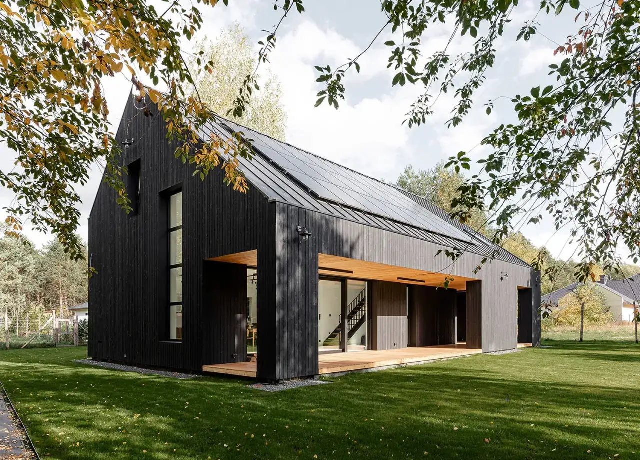 Nowoczesny dom z czarnego, opalane drewno, z panelami słonecznymi na dachu. Idealny przykład, czym pomalować opalane drewno, by uzyskać taki efekt.