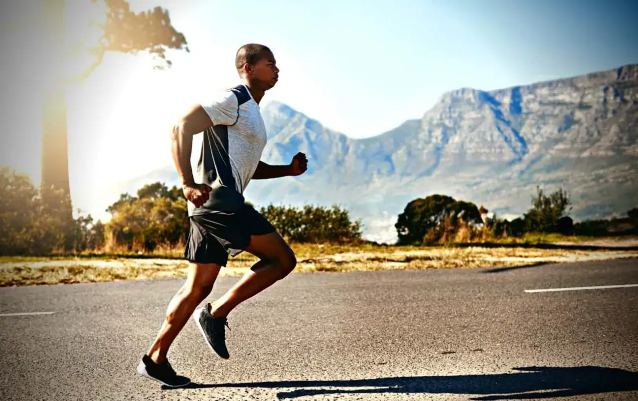 Mężczyzna w biegu, doskonale opanowana technika biegu, na tle gór i słońca.