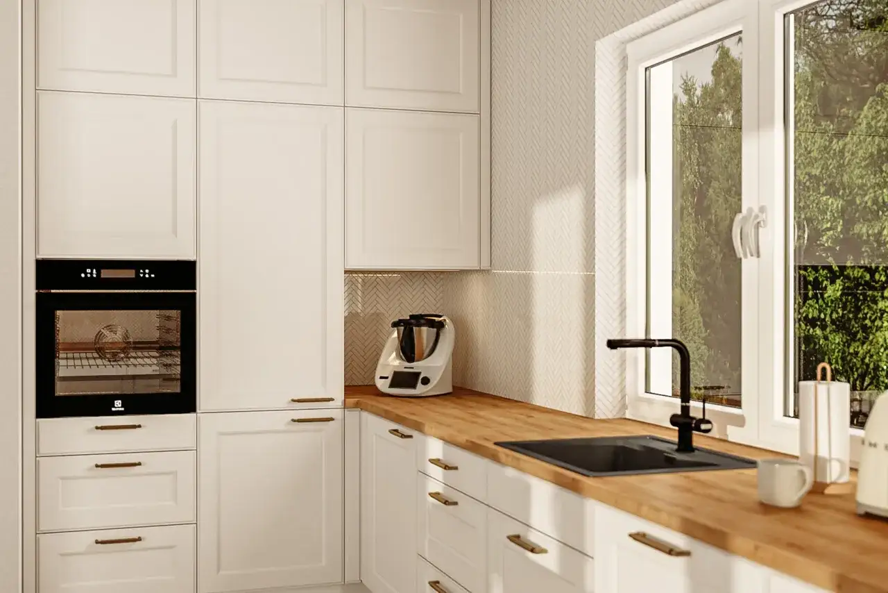 Jasna kuchnia z białymi meblami, wbudowanym piekarnikiem i okapem. Okna w kuchni są na standardowej wysokości, z widokiem na zieleń.