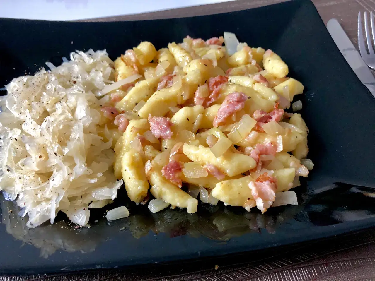 Gnocchi z boczkiem i cebulką, podane z kapustą kiszoną. Pyszne danie na talerzu.