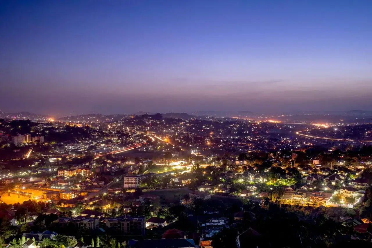 Rozświetlone wzg&oacute;rza stolicy Ugandy nocą, z migoczącymi światłami miasta i samochod&oacute;w na tle fioletowego nieba.