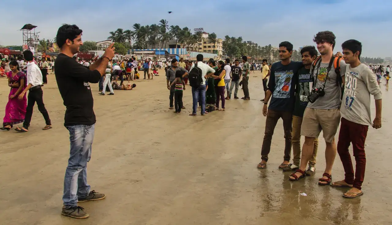 Tłum ludzi na plaży, jeden mężczyzna robi zdjęcie. Czy Indie są bezpieczne? Ludzie spacerują, bawią się, cieszą się słońcem.