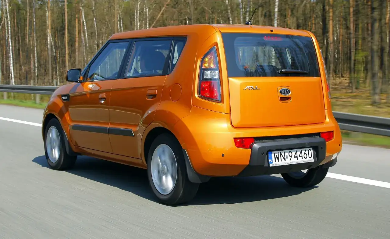 Pomarańczowy Kia Soul jedzie po drodze, otoczony lasem.
