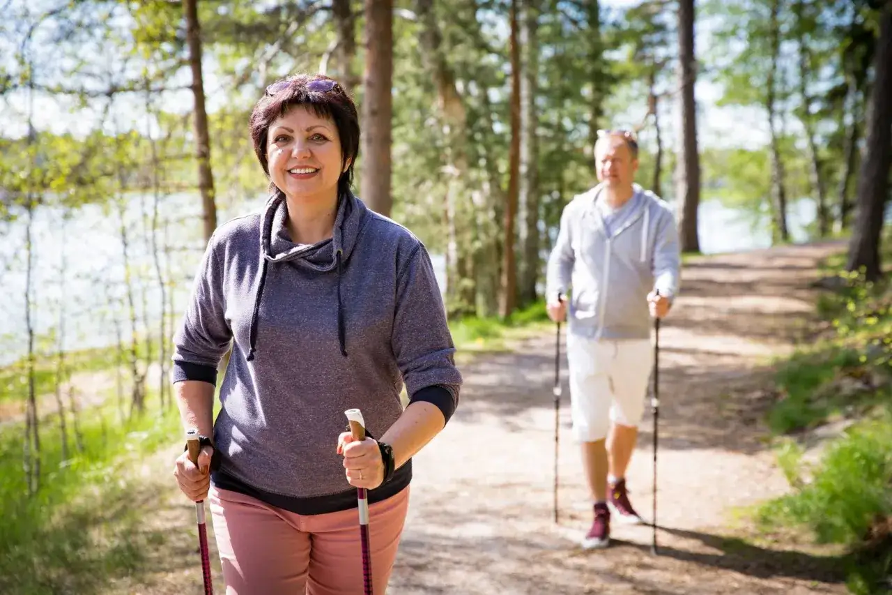 Uśmiechnięta kobieta i mężczyzna uprawiający nordic walking na leśnej ścieżce.
