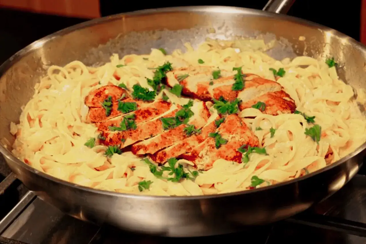 Pyszny kurczak alfredo przepis w sosie śmietanowym z tagliatelle, posypany świeżą natką pietruszki, gotowy do podania.