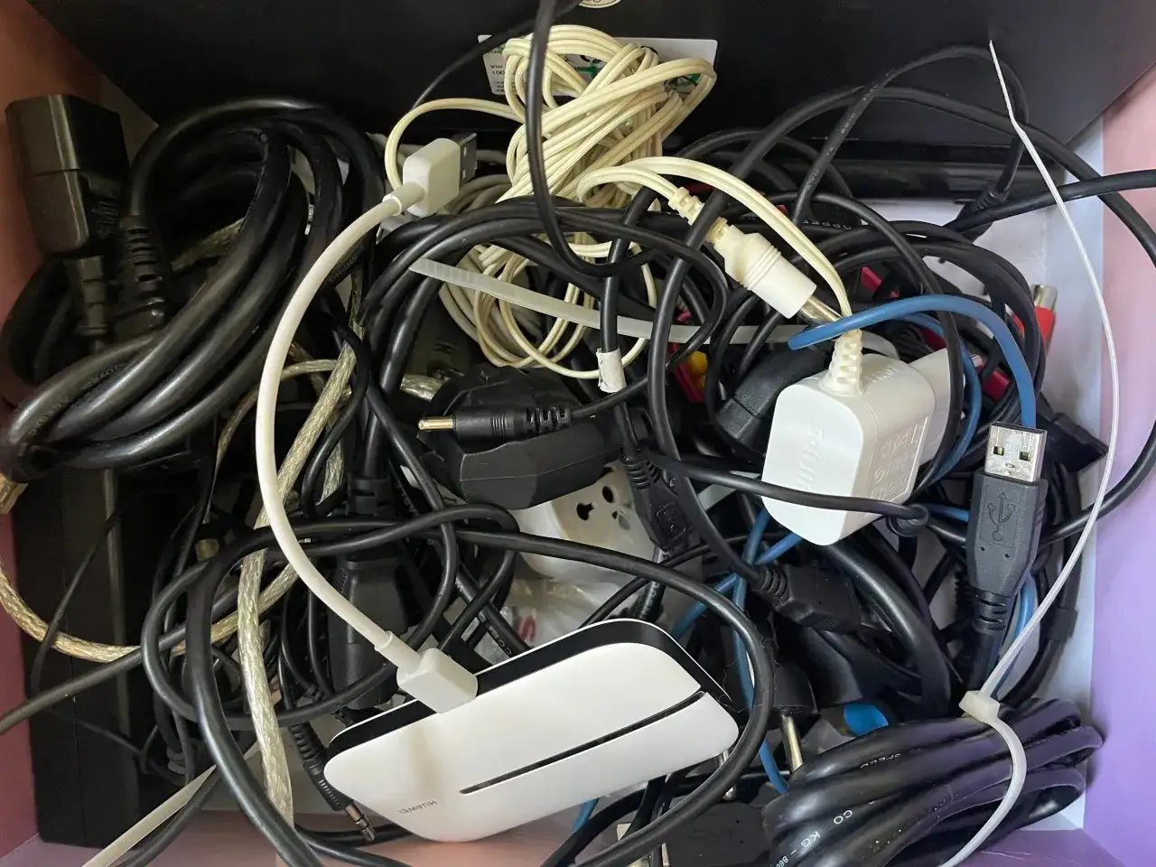 Plątanina kabli elektrycznych: czarne, białe i kremowe przewody tworzą chaos. Widać wtyczki, zasilacze i złącza USB.