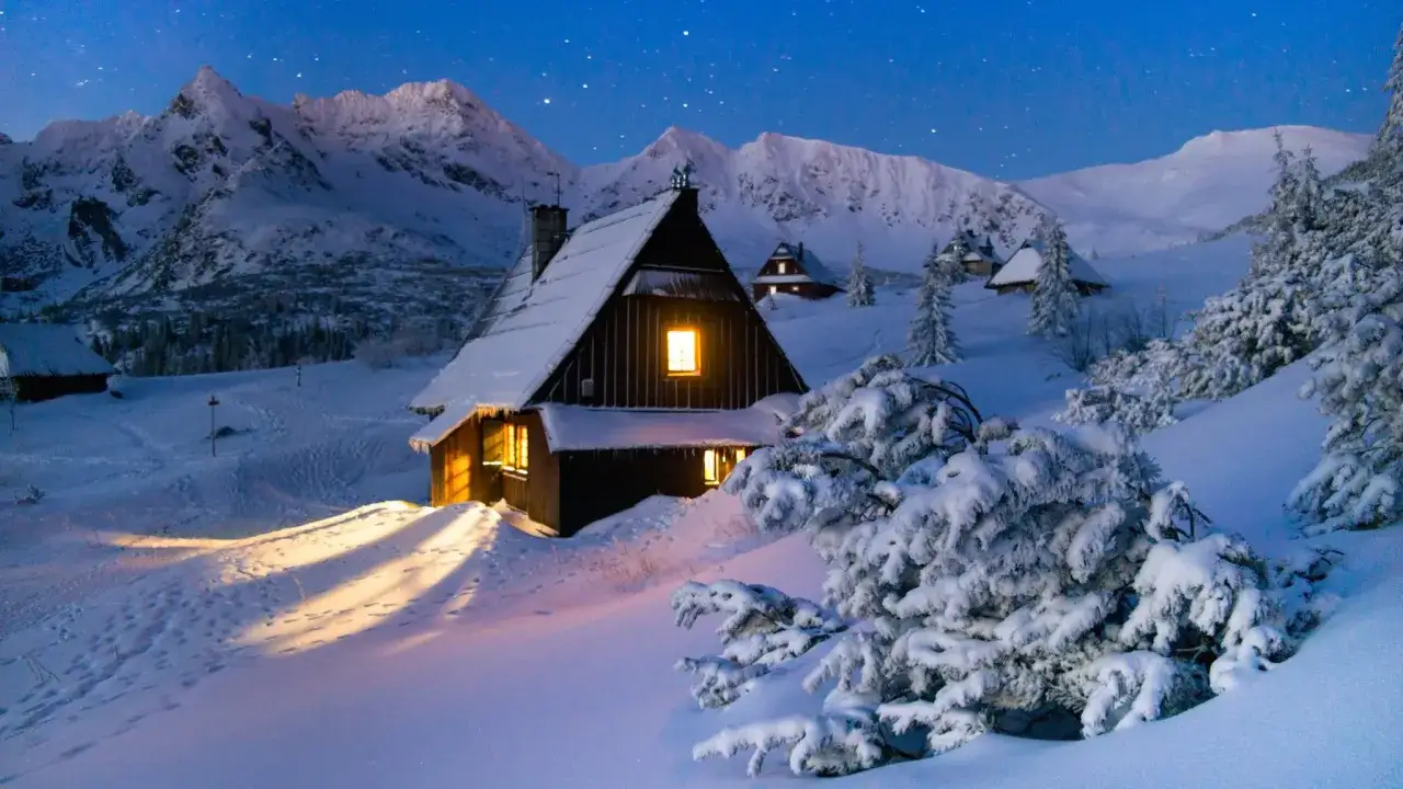 Zimowy szlak w Tatrach prowadzi do ośnieżonych chat. Widać g&oacute;ry, gwiazdy i ślady na śniegu.