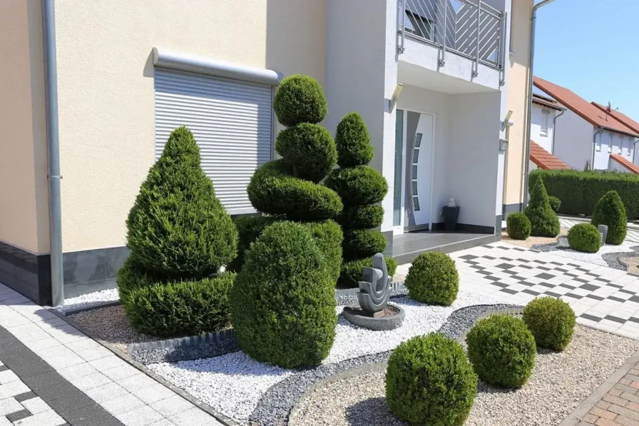 Piękne wzory kostki brukowej przed domem, otoczone starannie przyciętymi krzewami i drzewkami.