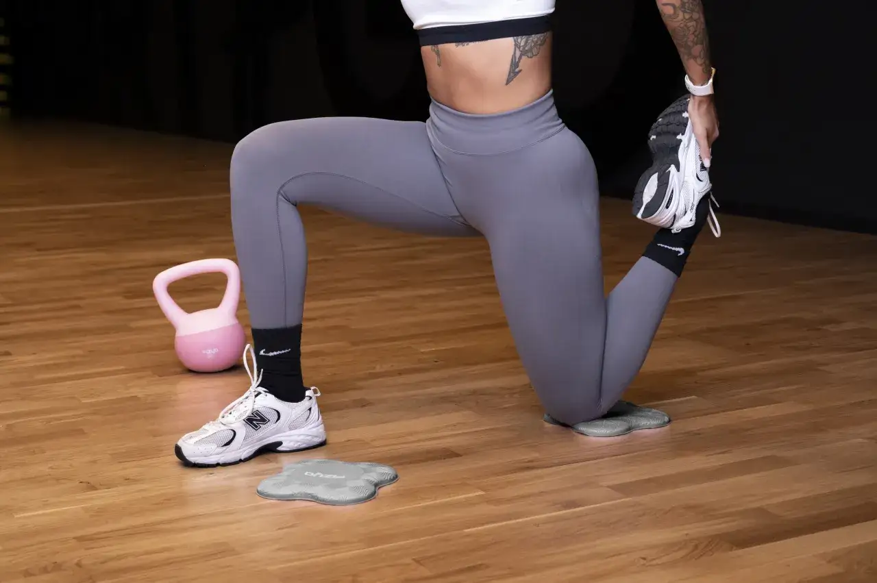 Kobieta w legginsach wykonuje ćwiczenia na podłodze. Obok leży różowa kettlebell. Ile powinien trwać trening na siłowni?