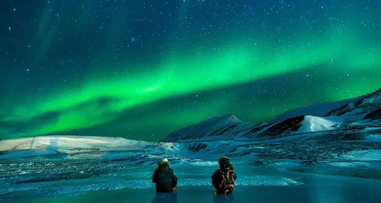 Dwie osoby siedzą na lodzie, podziwiając spektakularną zorzę polarną nad Tromsø.