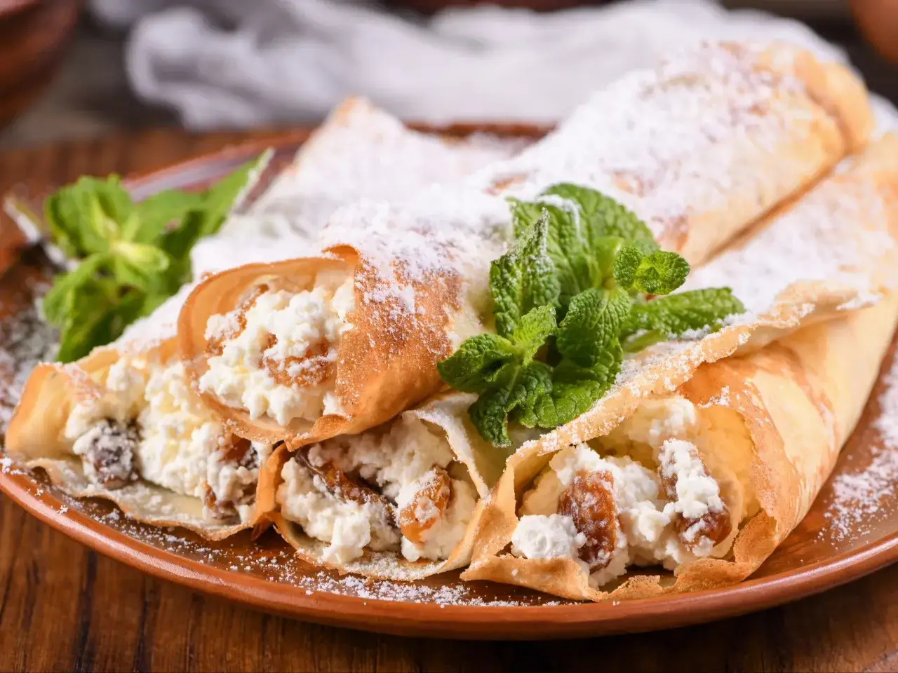 Naleśniki z serem na słodko, posypane cukrem pudrem i udekorowane miętą. Pyszna alternatywa dla wersji z mięsem i grzybami.