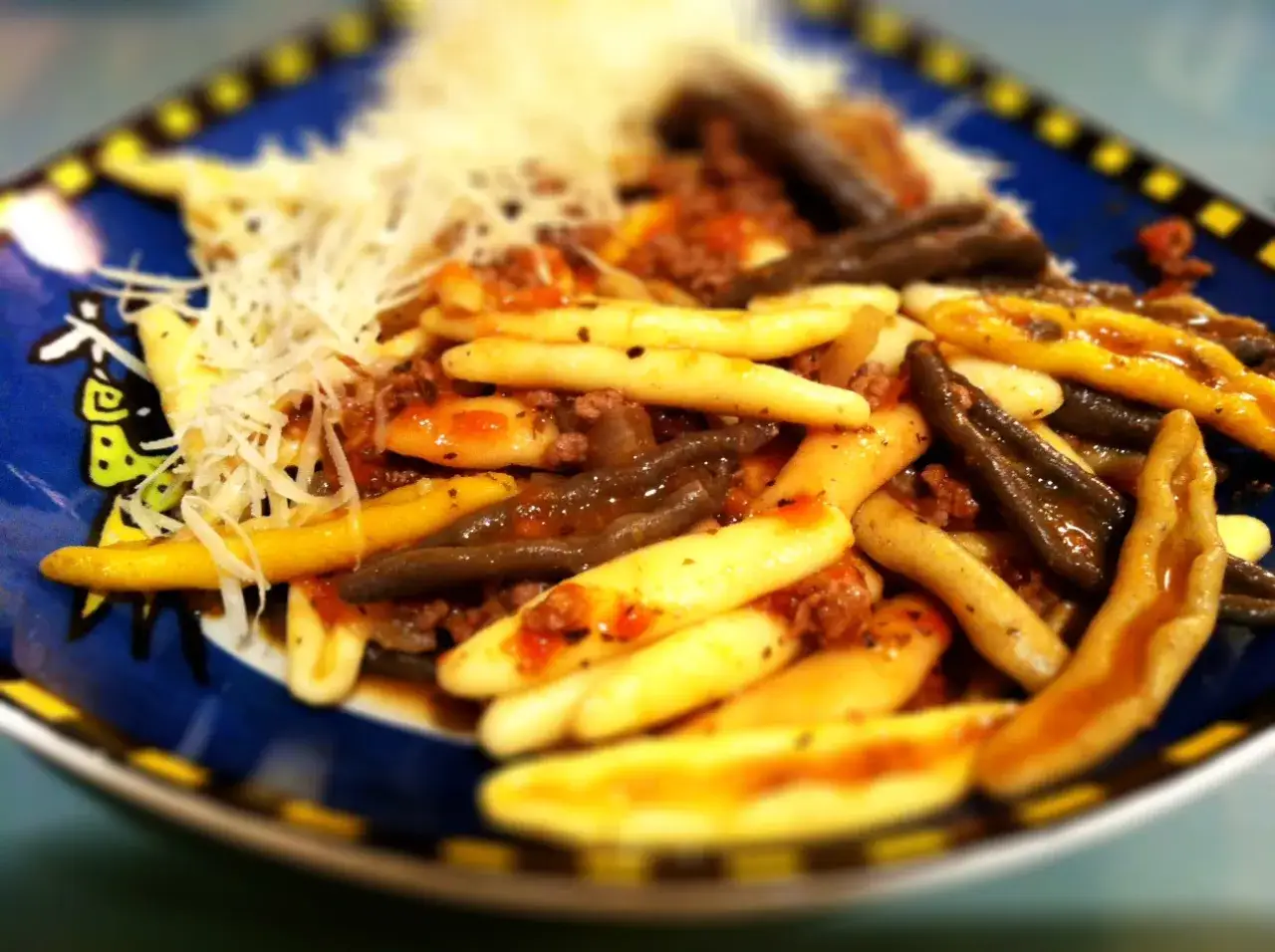 Kluski vs makaron: danie z kluskami w sosie bolońskim, posypane parmezanem. Różne rodzaje klusek, niektóre żółte, inne ciemne.