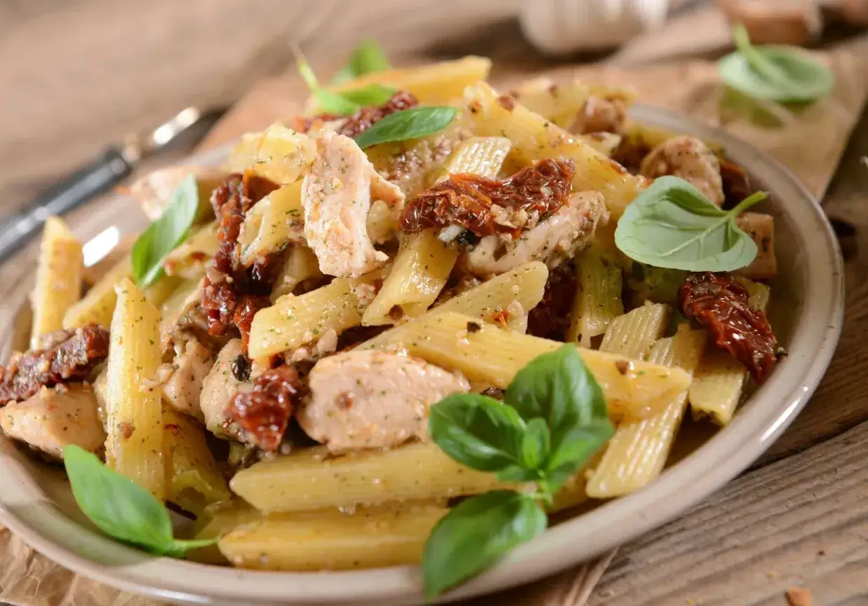 Penne z kurczakiem i suszonymi pomidorami, ozdobione listkami bazylii. Pyszne danie na obiad.
