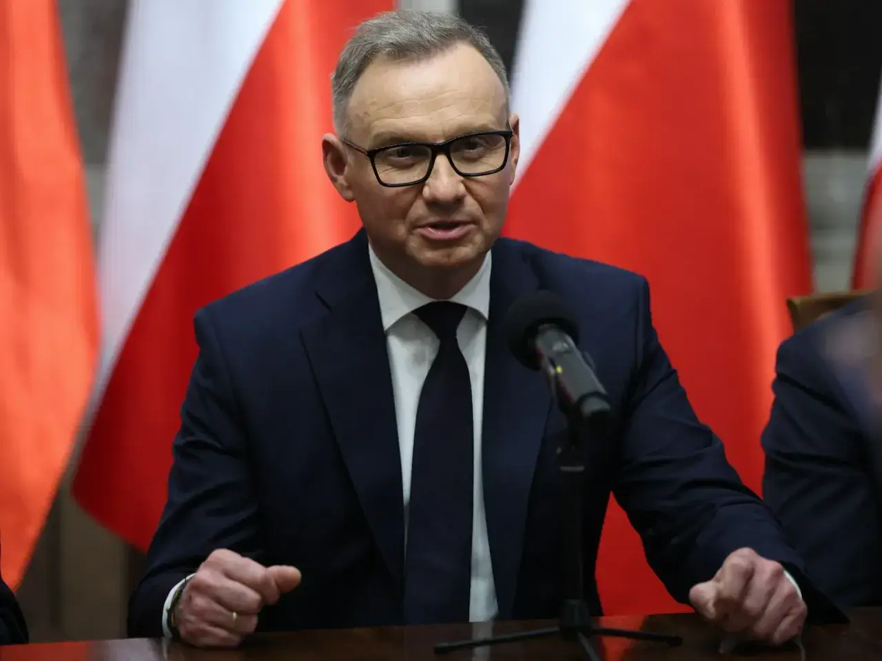Andrzej Duda w okularach, w garniturze, przemawia przy mikrofonie na tle flag. Czy planuje karierę w strukturach międzynarodowych po zakończeniu kadencji?