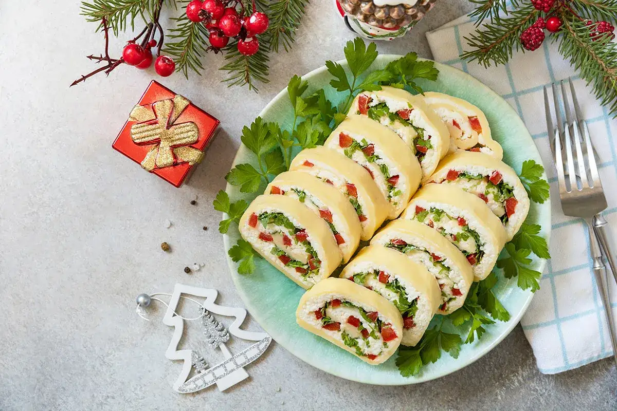 Roladki z sera z papryką i ziołami na talerzu, idealne jako inspiracja, co ugotować na Wigilię. Obok świąteczne dekoracje.