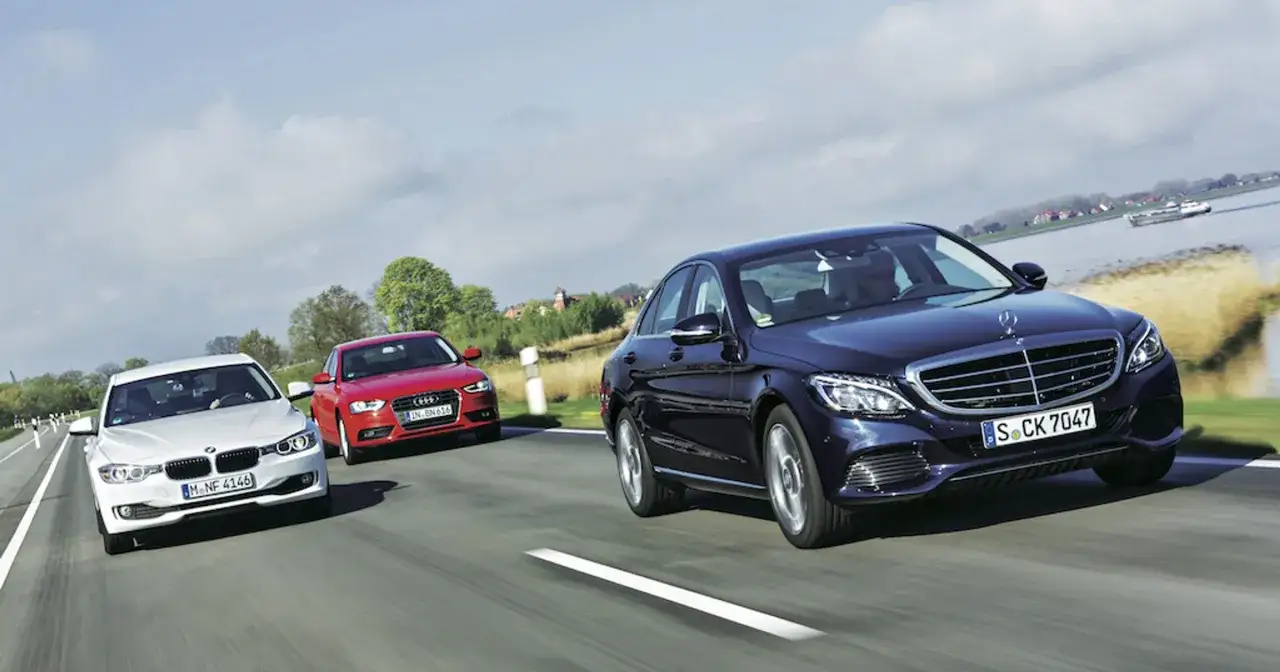 Trzy samochody: ciemnoniebieski Mercedes Klasy C, czerwone Audi i białe BMW jadą drogą. Dane techniczne Mercedes C Klasa są kluczowe dla porównania.