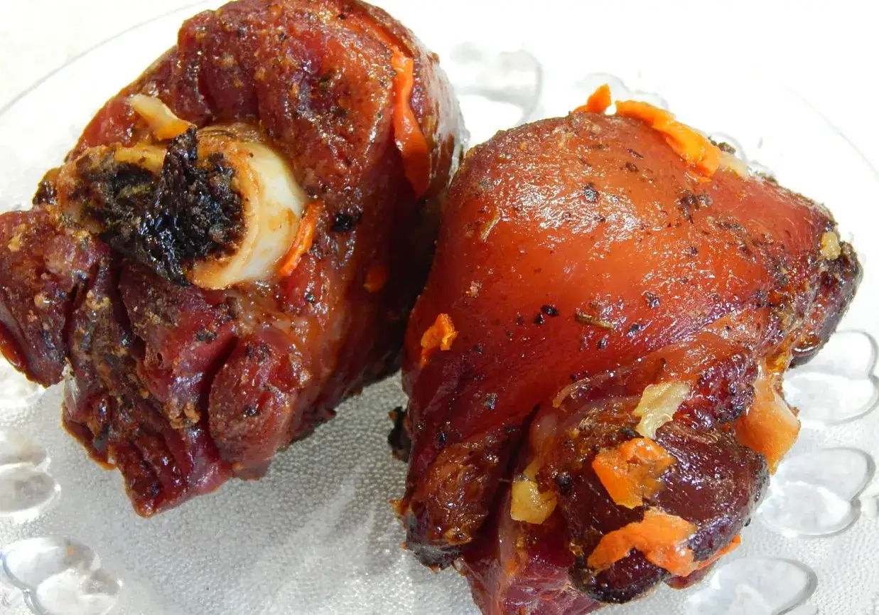 Dwie soczyste, najlepsza golonka gotowana i pieczona, błyszczące od sosu, z widocznymi kawałkami marchewki i przypraw.