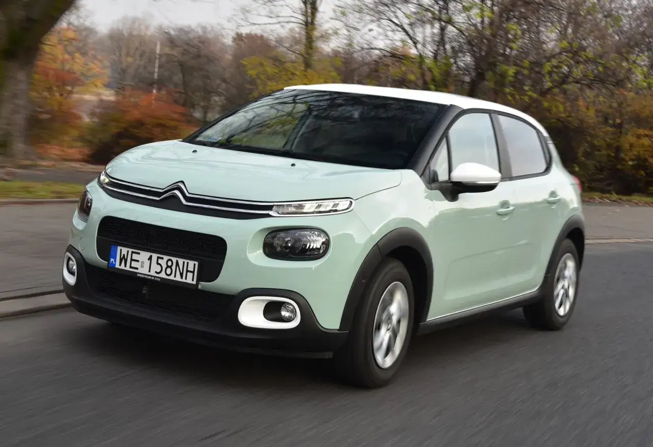 Jasnozielony Citroen C3 z białym dachem, idealne auto do 40 tys. zł, jedzie po drodze wśród jesiennych drzew.