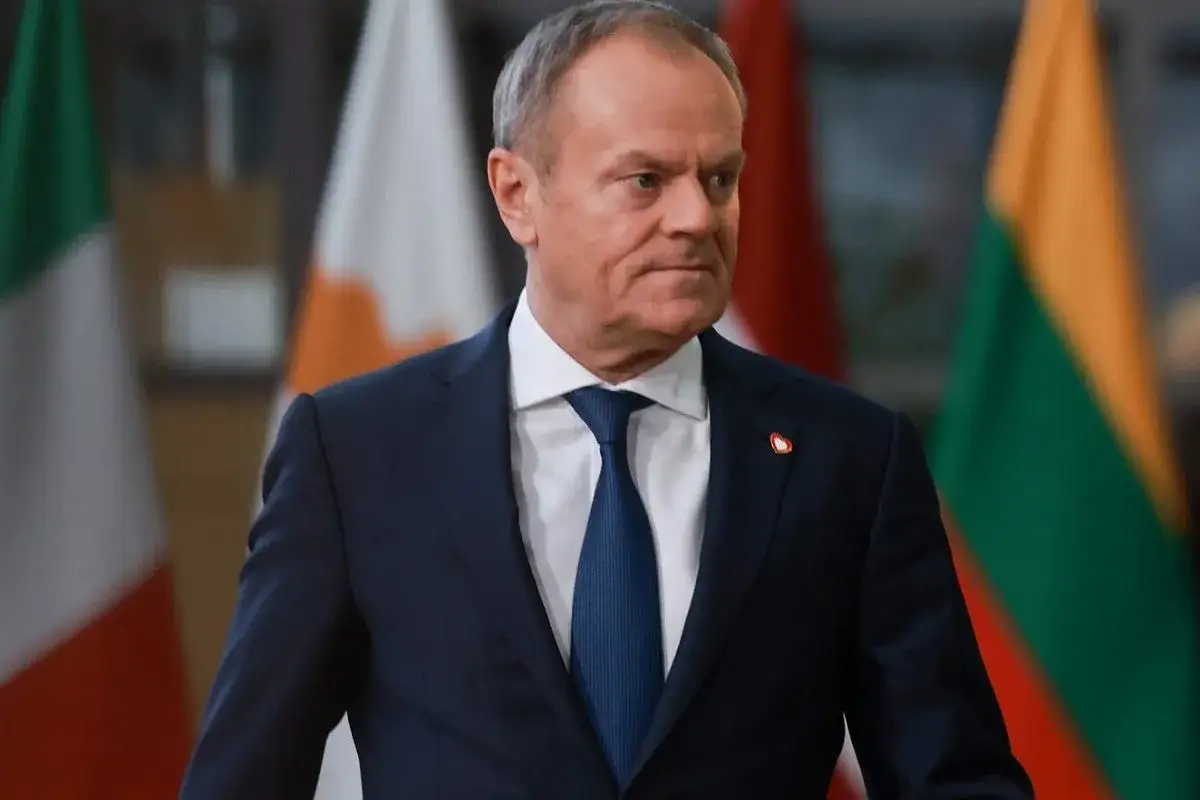 Donald Tusk w garniturze, na tle flag państwowych. Zastanawiamy się, co zrobił Tusk dla Polski.