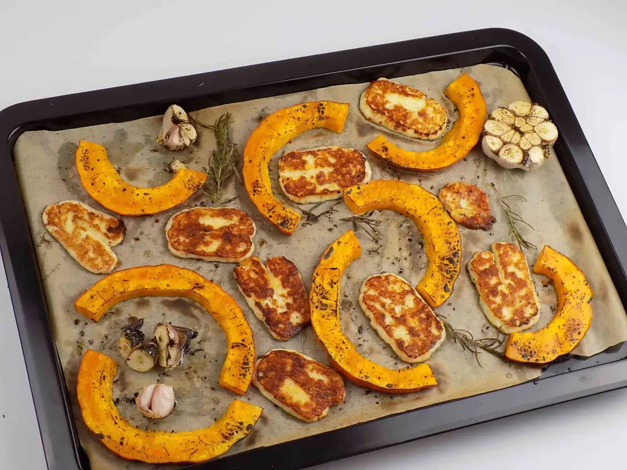 Na blasze upieczone kawałki dyni hokkaido, ser halloumi i czosnek.