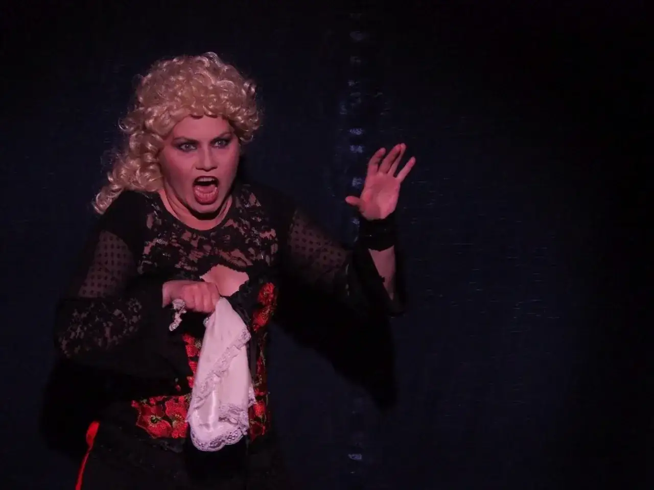 Sylwia Janowicz-Dobrowolska w dramatycznej scenie, z rozwianymi blond włosami i wykrzywionymi ustami, trzyma białą chusteczkę.