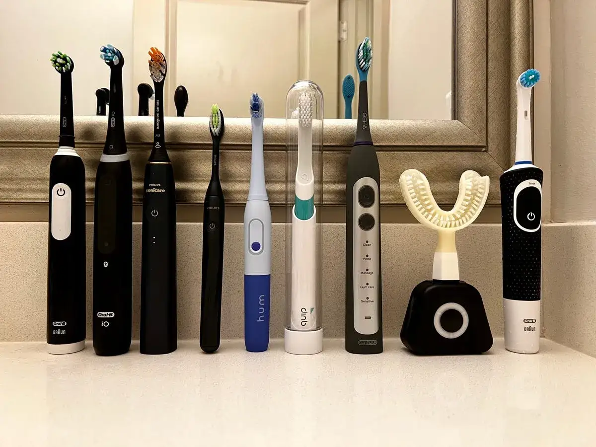 Jaka szczoteczka soniczna? Rząd elektrycznych szczoteczek do zębów, w tym Oral-B, Philips Sonicare, Hum i Quip, ustawionych na blacie łazienkowym.
