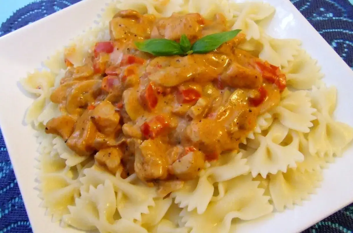 Pyszny makaron farfalle z kremowym sosem paprykowym i kawałkami kurczaka, udekorowany listkiem bazylii.