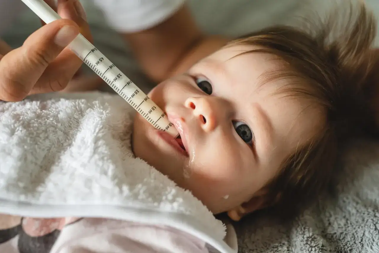 Jak podać dziecku antybiotyk żeby nie wypluło? Strzykawka z lekiem trafia prosto do buzi malucha, który ma na szyi ręcznik.