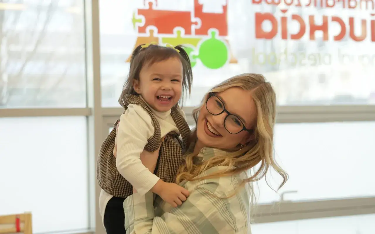 Uśmiechnięta opiekunka trzyma dziecko. Zastanawiasz się, ile kosztuje żłobek w Warszawie?