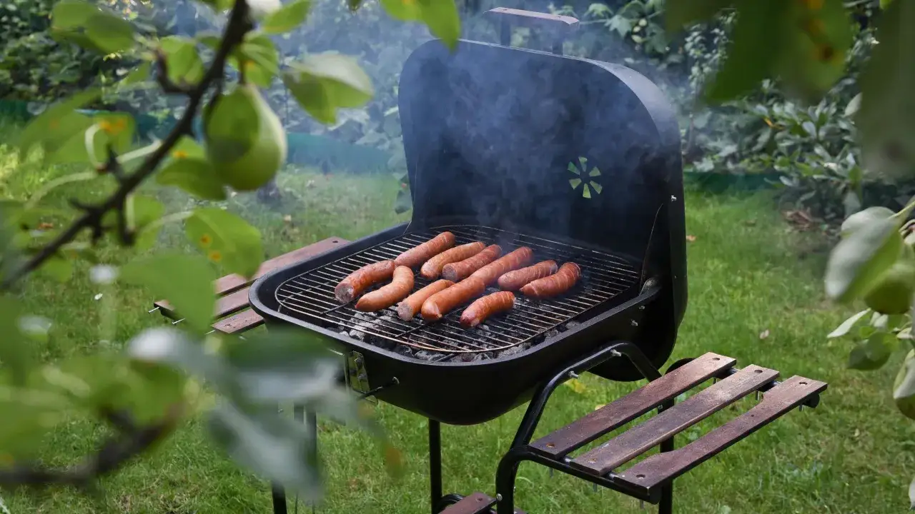 Kiełbaski skwierczą na grillu w ogrodzie. Idealne miejsce, gdzie zrobić grilla i cieszyć się latem.