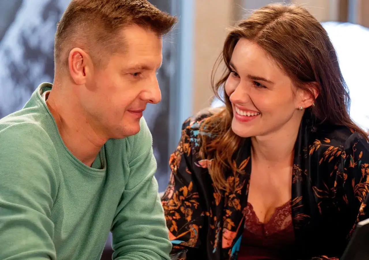 Uśmiechnięta para, czy Frania odchodzi z M jak Miłość? Mężczyzna w zielonej bluzie i kobieta w kwiecistej narzutce patrzą na siebie z czułością.