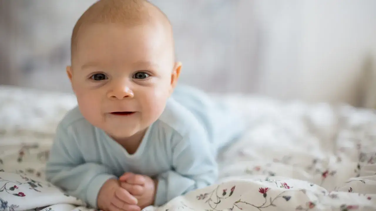 Uśmiechnięte niemowlę na brzuchu, być może przeżywające skok rozwojowy 6 tydzień objawy.