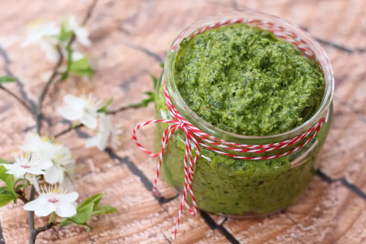 Słoik domowego pesto z czosnku niedźwiedziego, ozdobiony sznurkiem, obok gałązki kwitnącej wiśni.