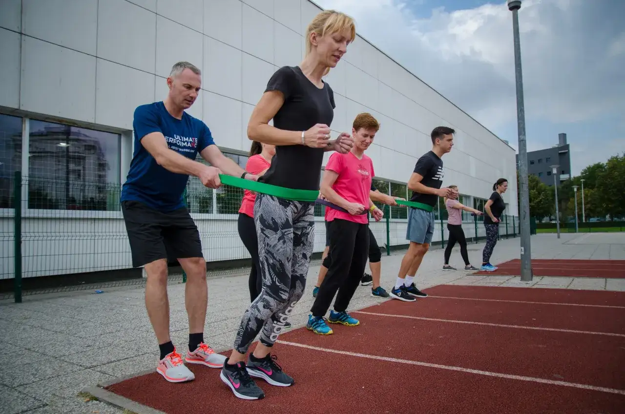 Grupa ćwiczy technikę biegu na bieżni, używając taśmy oporowej do wzmocnienia mięśni.