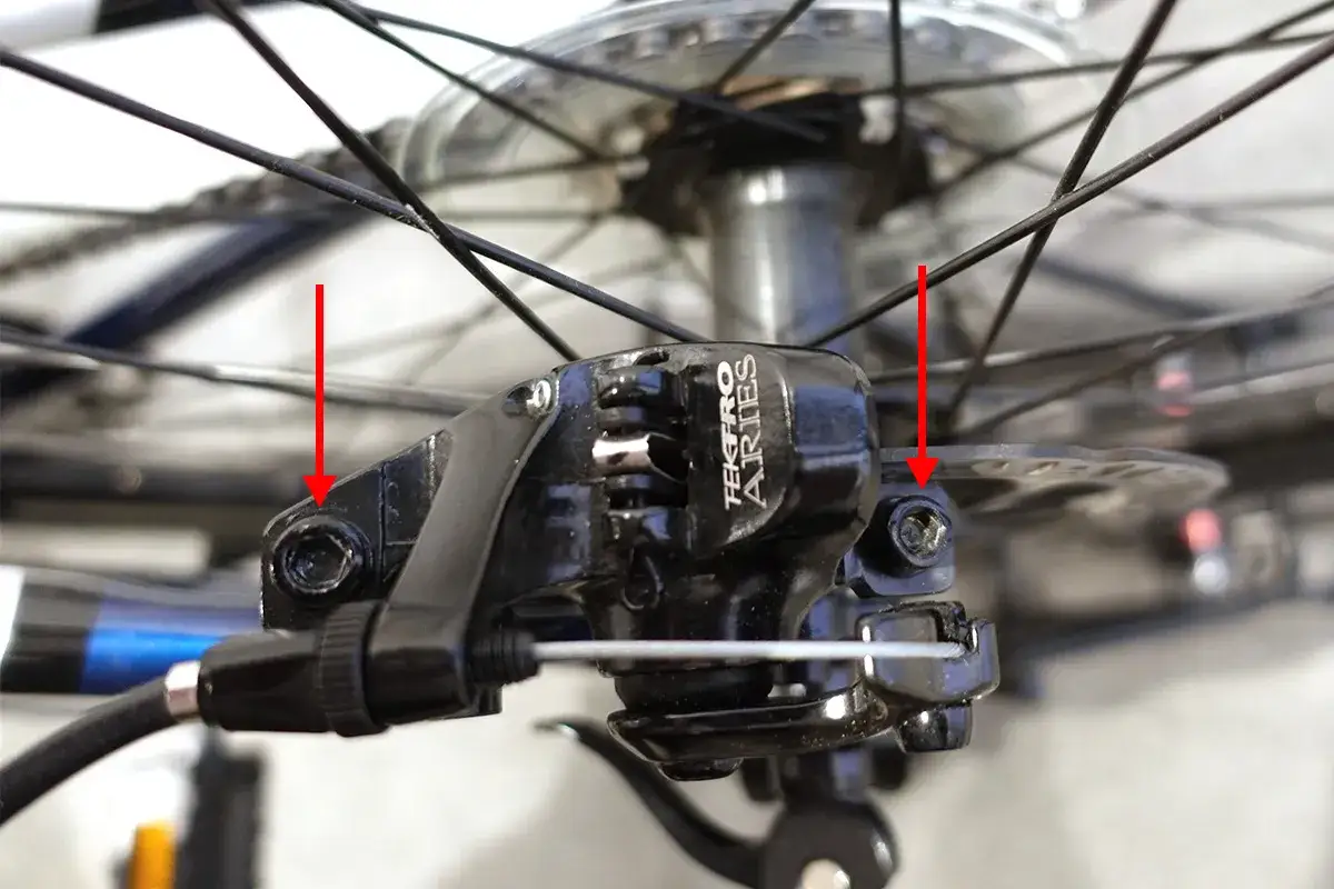 Regulacja hamulców hydraulicznych w rowerze: czerwone strzałki wskazują śruby do centrowania zacisku hamulcowego Tektro Aries.